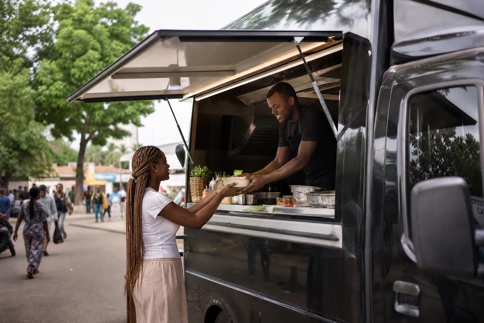Food truck en bord de rue : le cuisinier tend un plat à une cliente par le passe-plat.