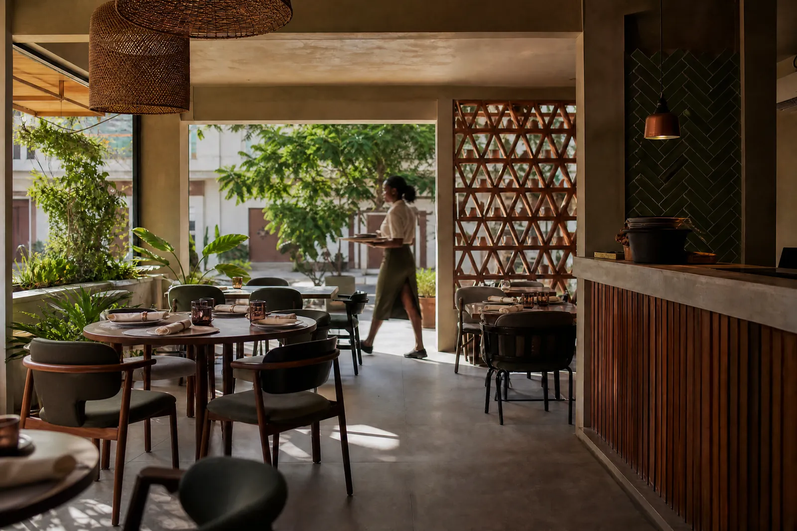 Salle de restaurant dressée, une serveuse traverse avec un plateau.